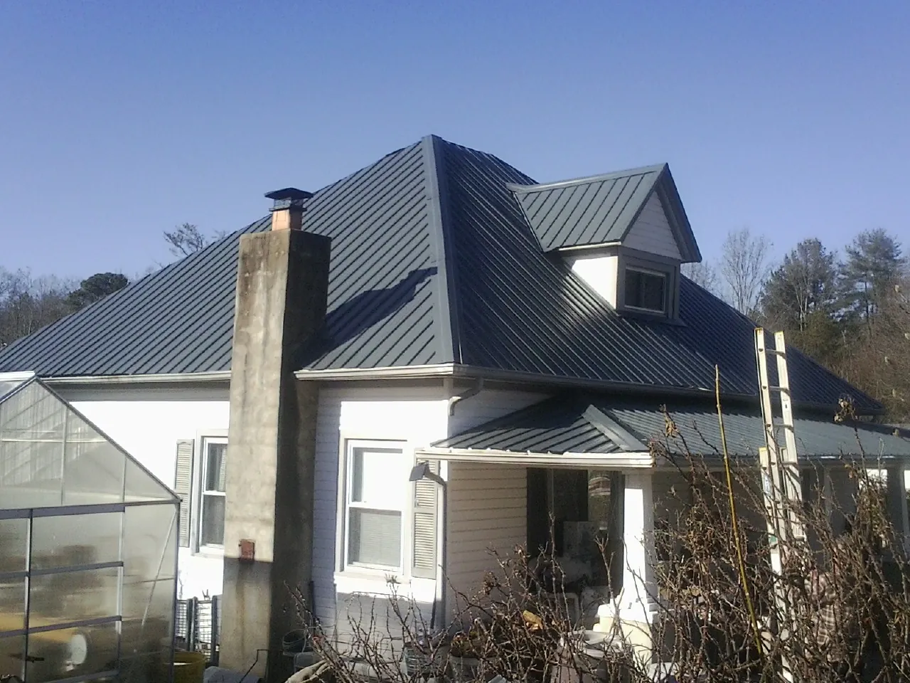 Dark blue standing seam metal roof on a white farmhouse with dormer — Slate & Tile Roof Repair by Roofing Brothers in Perris