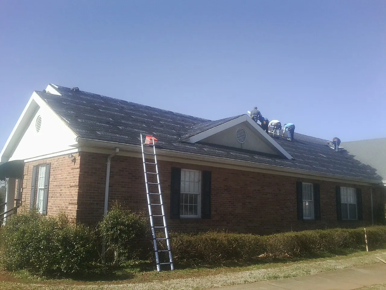 Crew tearing shingles off a brick ranch roof with a ladder set — Emergency Roof Repair work by our crew in Perris
