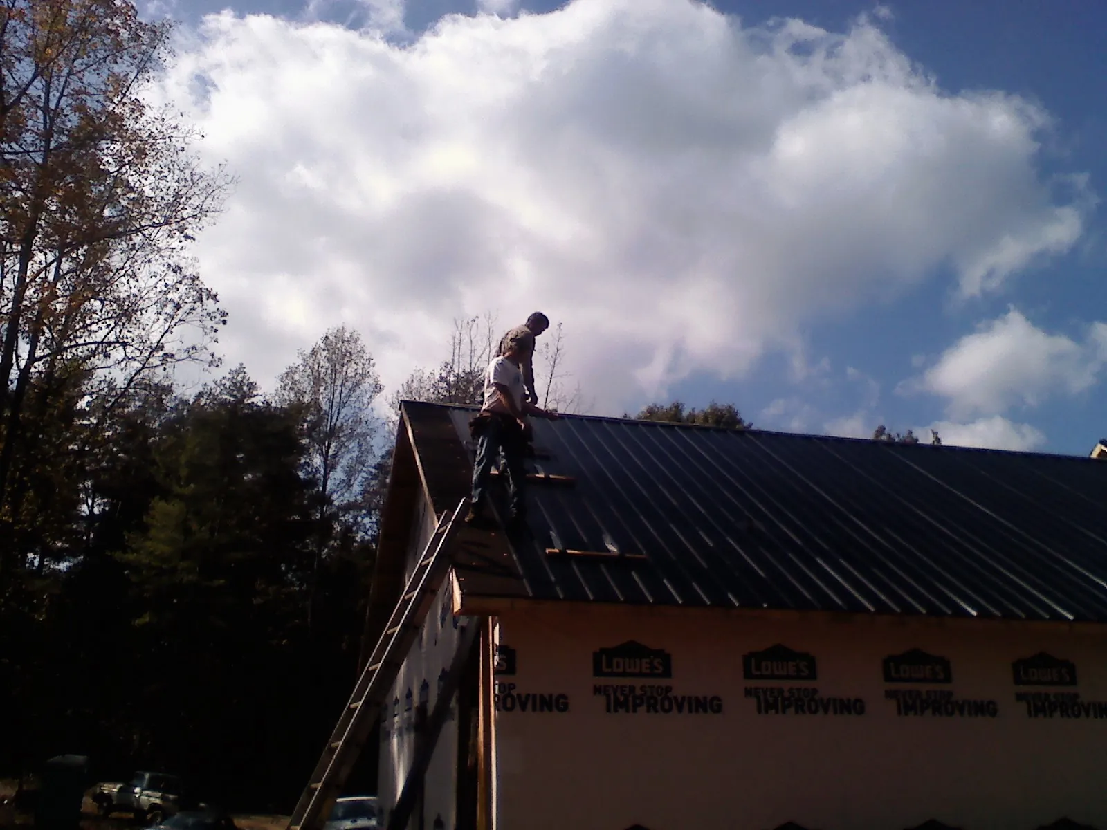 Roofer fastening dark metal panels high against a cloudy sky, from a Roof Inspection job in Perris
